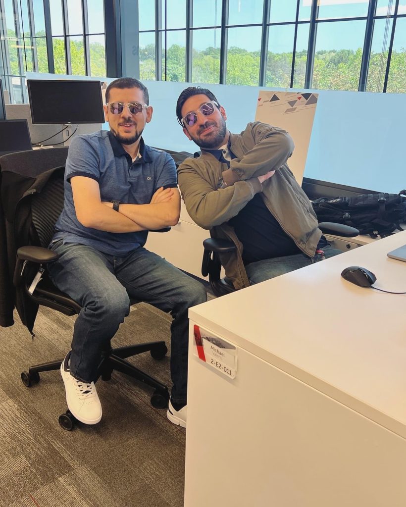 Two male employees sitting at a desk wearing icims branded sunglasses
