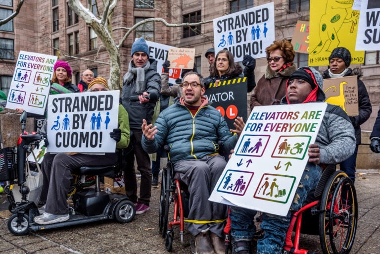 A group of wheelchair users and allies holding protest signs in NYC that say Stranded by Cuomo and Elevators are for Everyone
