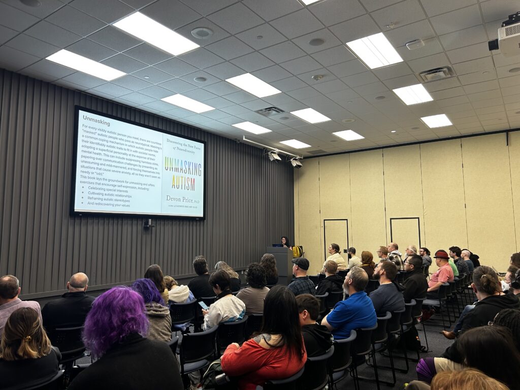 Speaker Sharyn Morrow standing behind a tall podium while presenting to a full room of attendees.