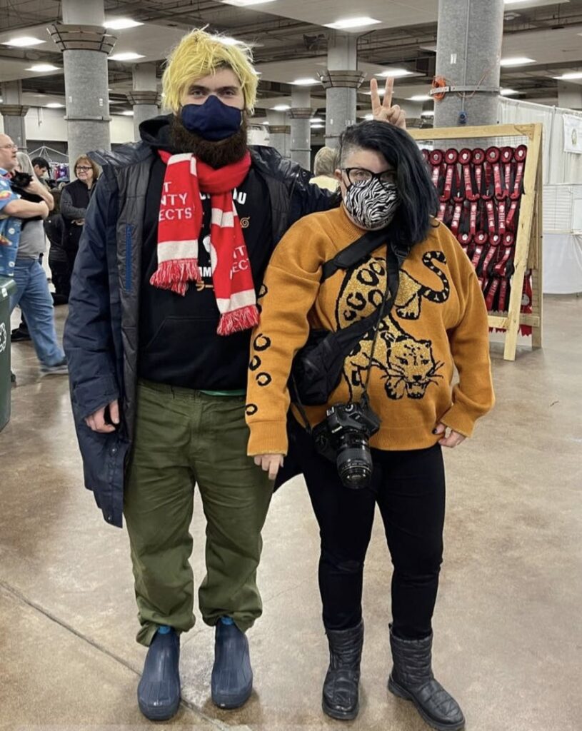 A young autistic man wearing a KN95 mask posing for a photo with their AuDHD parent who is also wearing a mask.